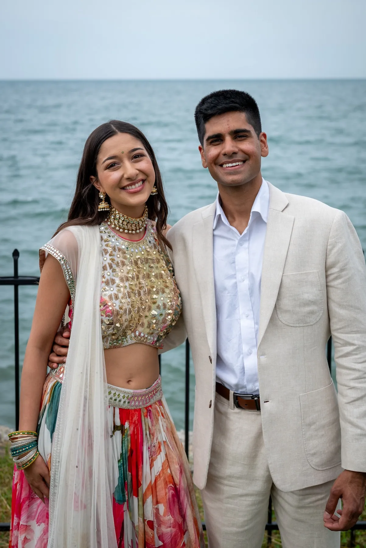 Alisha and Kunal standing together beside the water, dressed for their engagement